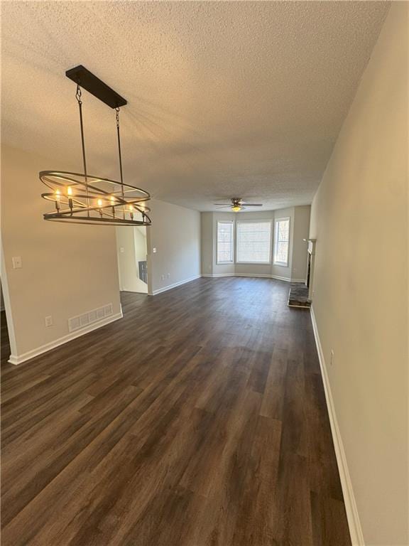 unfurnished living room with visible vents, baseboards, dark wood finished floors, ceiling fan with notable chandelier, and a textured ceiling