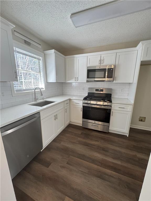 kitchen with a sink, dark wood-style floors, stainless steel appliances, white cabinets, and light countertops