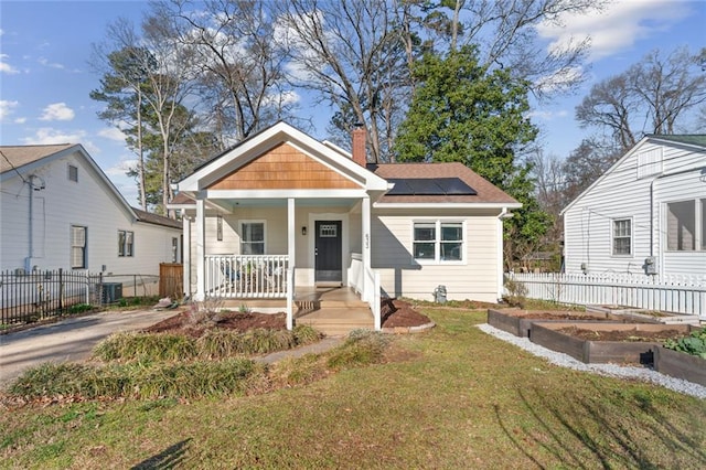 view of front of property with a porch, fence, a garden, roof mounted solar panels, and a front yard