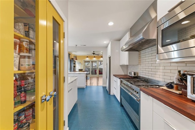 kitchen with white cabinets, wooden counters, appliances with stainless steel finishes, wall chimney range hood, and tasteful backsplash