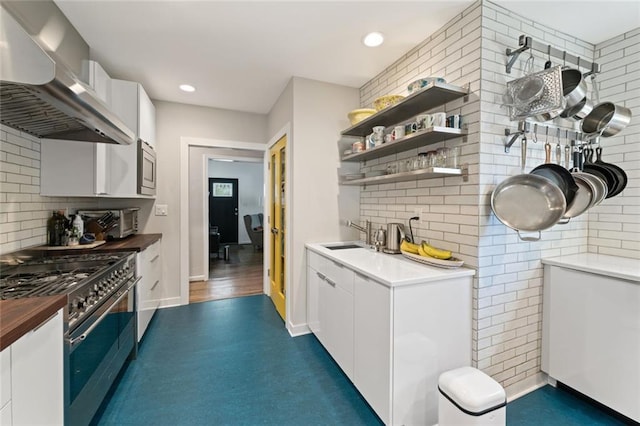 kitchen with wall chimney exhaust hood, appliances with stainless steel finishes, a sink, white cabinetry, and backsplash