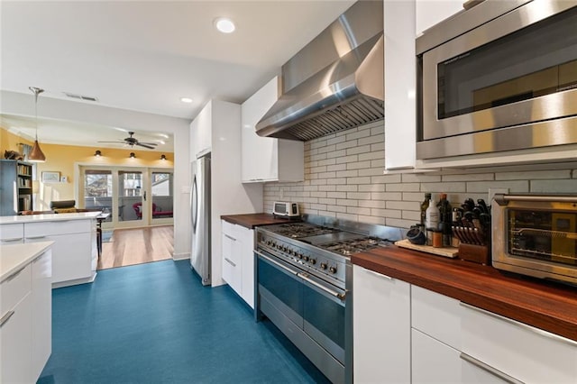 kitchen featuring appliances with stainless steel finishes, butcher block countertops, visible vents, and wall chimney exhaust hood