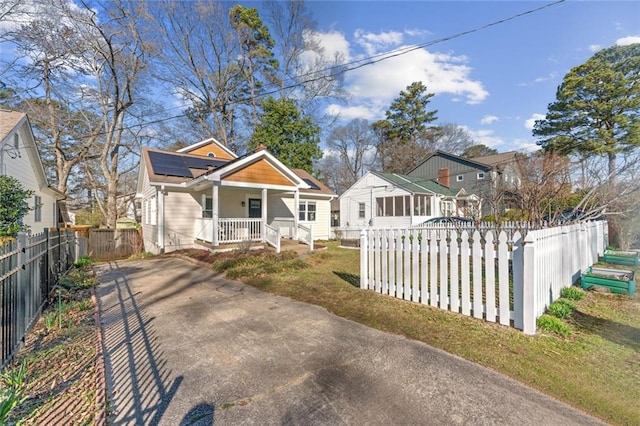 bungalow-style home with a porch, roof mounted solar panels, and a fenced front yard