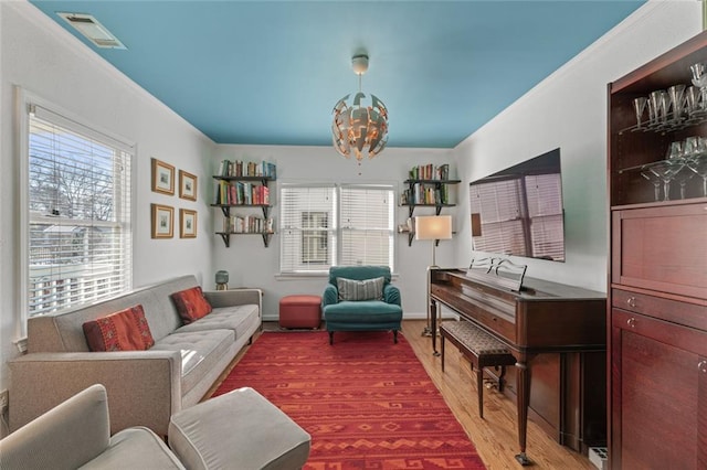 living room with visible vents, ornamental molding, wood finished floors, a chandelier, and baseboards