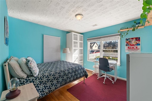 bedroom featuring a textured ceiling, wood finished floors, visible vents, and baseboards