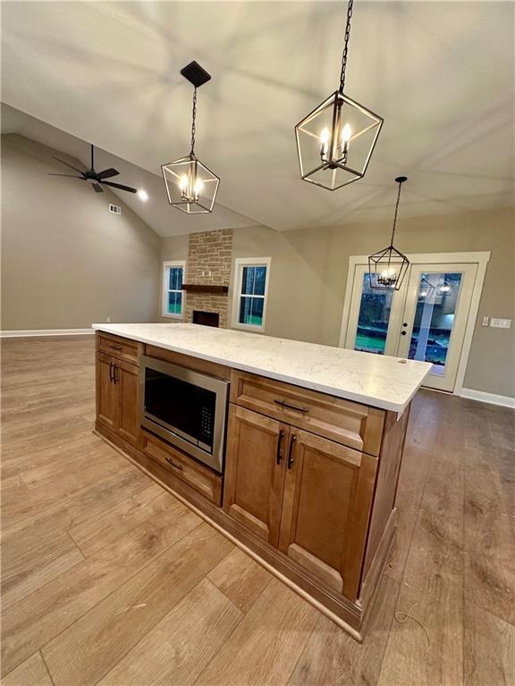 kitchen with stainless steel microwave, wood finished floors, open floor plan, brown cabinetry, and lofted ceiling