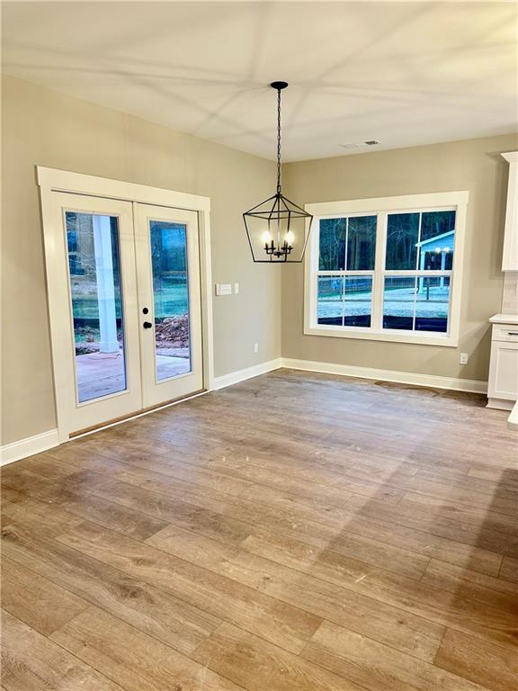 unfurnished dining area featuring an inviting chandelier, french doors, baseboards, and wood finished floors