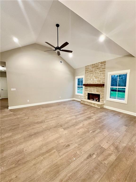 unfurnished living room with vaulted ceiling, wood finished floors, baseboards, and ceiling fan