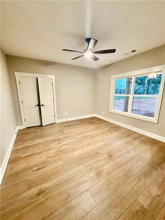 unfurnished room with light wood finished floors, a ceiling fan, and baseboards