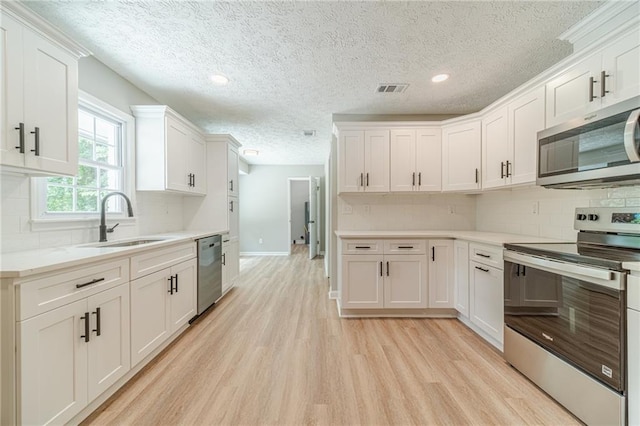 kitchen with appliances with stainless steel finishes, a sink, light wood-style floors, a textured ceiling, and tasteful backsplash