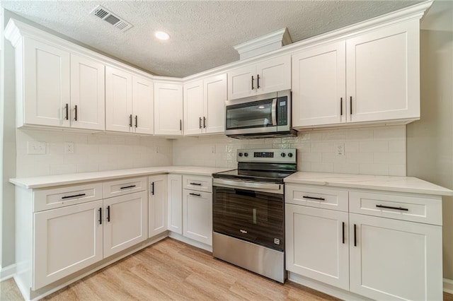 kitchen with stainless steel appliances, light wood-style flooring, white cabinets, a textured ceiling, and tasteful backsplash