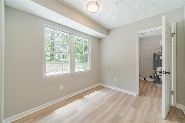 unfurnished room with gas water heater, light wood-type flooring, a textured ceiling, and baseboards