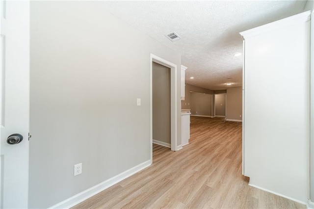 corridor with a textured ceiling, light wood finished floors, and baseboards