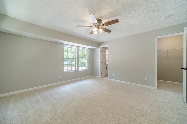 unfurnished bedroom featuring a textured ceiling, light colored carpet, baseboards, and a walk in closet