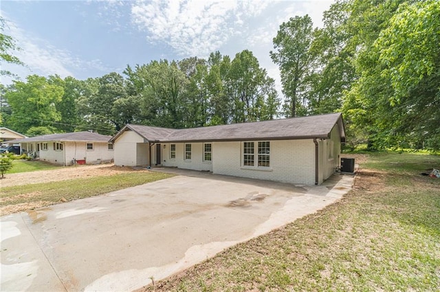 ranch-style home featuring driveway, brick siding, cooling unit, a front yard, and view of wooded area