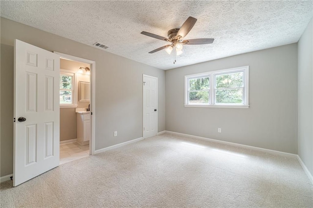 unfurnished bedroom with light carpet, baseboards, a textured ceiling, connected bathroom, and ceiling fan