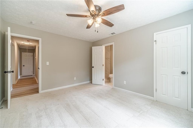unfurnished bedroom with attic access, light colored carpet, baseboards, a textured ceiling, and connected bathroom