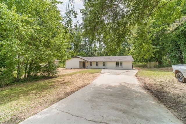 ranch-style home featuring asphalt driveway, a front lawn, and view of wooded area