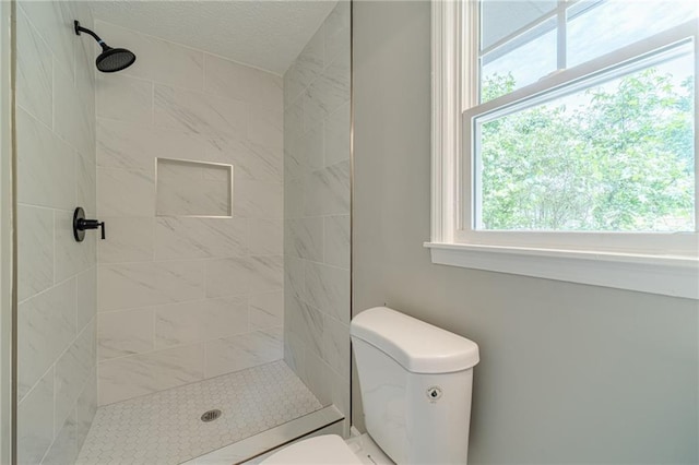 bathroom with toilet, tiled shower, and a textured ceiling