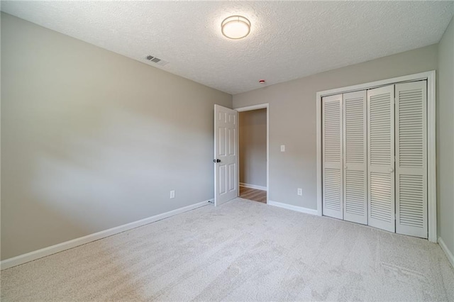 unfurnished bedroom with carpet floors, a textured ceiling, a closet, and baseboards