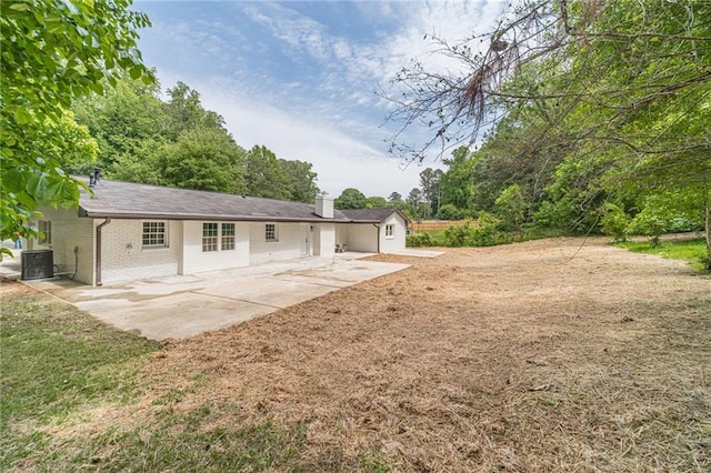 back of house with a patio, a chimney, brick siding, cooling unit, and a yard