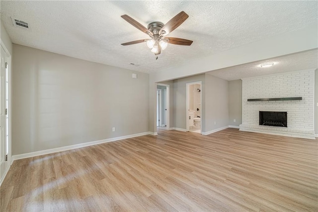 unfurnished living room with a textured ceiling, light wood-type flooring, ceiling fan, baseboards, and a brick fireplace