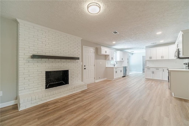 unfurnished living room with baseboards, light wood finished floors, a fireplace, a sink, and a textured ceiling