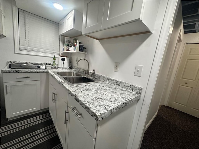 kitchen featuring white cabinetry, sink, light stone counters, and dark colored carpet