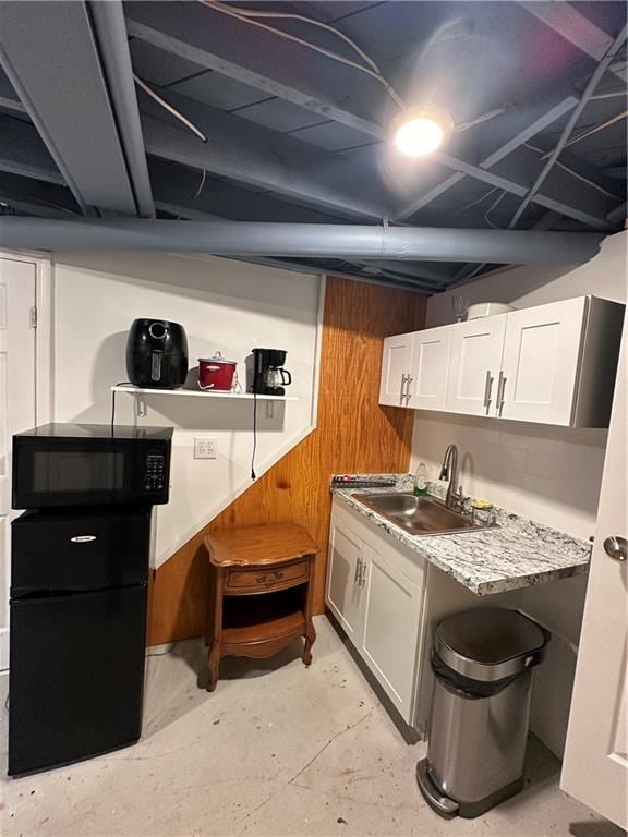 kitchen with white cabinets, wood walls, light stone countertops, and sink