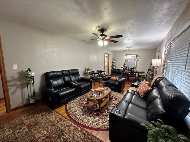 living room featuring ceiling fan with notable chandelier, a textured ceiling, and hardwood / wood-style flooring