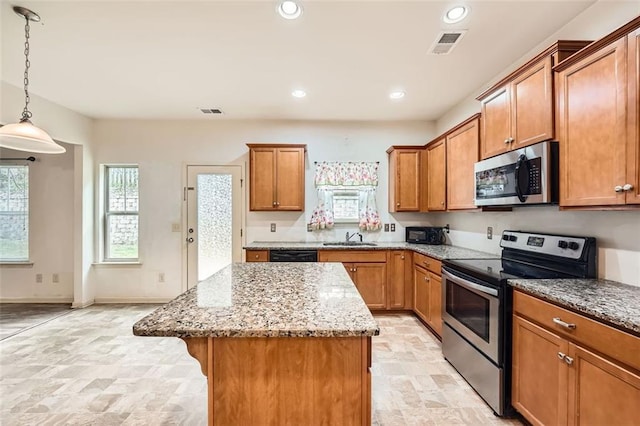 kitchen with visible vents, a center island, brown cabinets, stainless steel appliances, and light stone counters