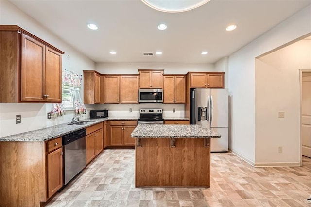kitchen with brown cabinetry, recessed lighting, stainless steel appliances, a kitchen island, and light stone counters