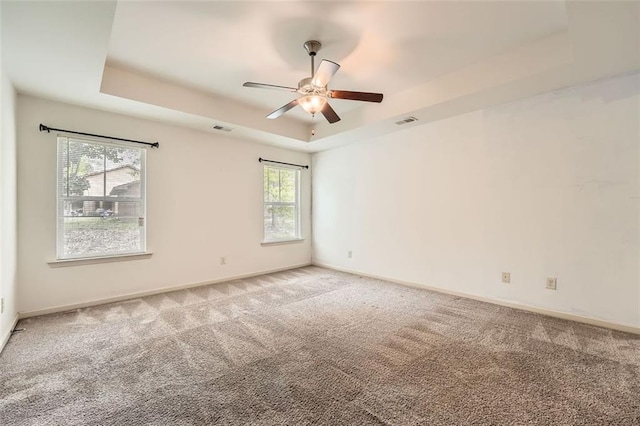 spare room featuring visible vents, baseboards, a raised ceiling, a ceiling fan, and light colored carpet