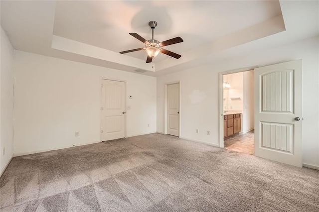 unfurnished bedroom with baseboards, a raised ceiling, ensuite bath, and light carpet
