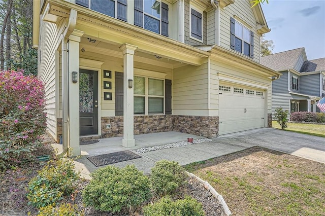 entrance to property with a porch, an attached garage, driveway, and stone siding