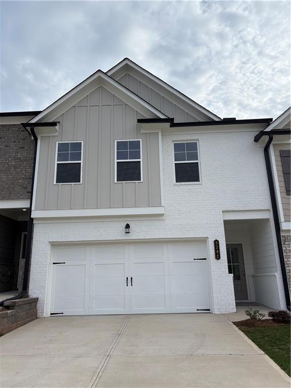 view of front of property featuring board and batten siding, a garage, driveway, and brick siding
