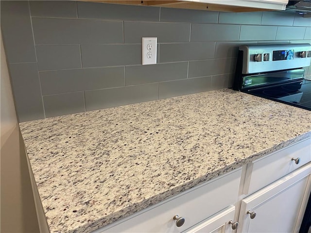 kitchen view of decorative backsplash, stainless steel range with electric stovetop, white cabinets, and light stone countertops