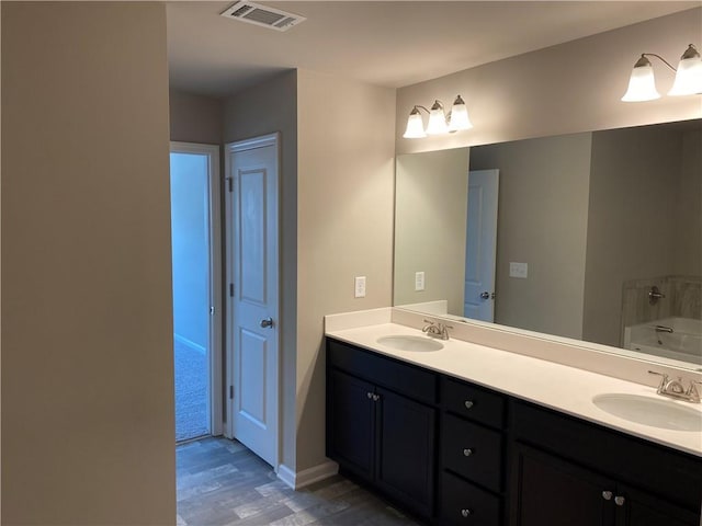 full bathroom featuring wood finished floors, double vanity, a tub, and baseboards