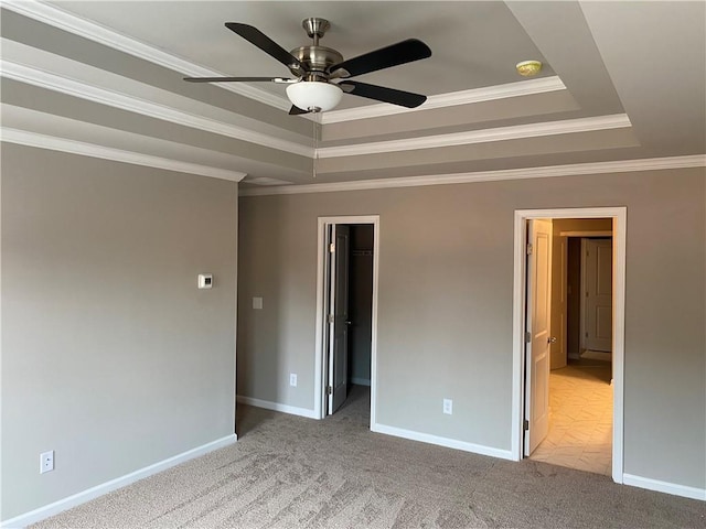 unfurnished bedroom with a tray ceiling, ornamental molding, carpet floors, a spacious closet, and baseboards