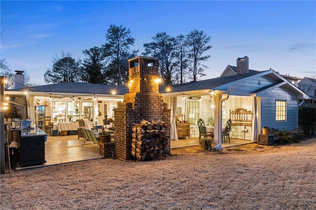 patio terrace at dusk with an outdoor brick fireplace, grilling area, and an outdoor kitchen