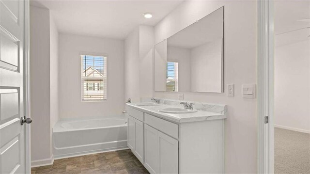full bathroom featuring a sink, a bath, double vanity, and baseboards