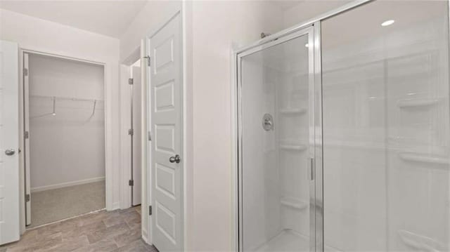 bathroom with a spacious closet, a shower stall, and baseboards