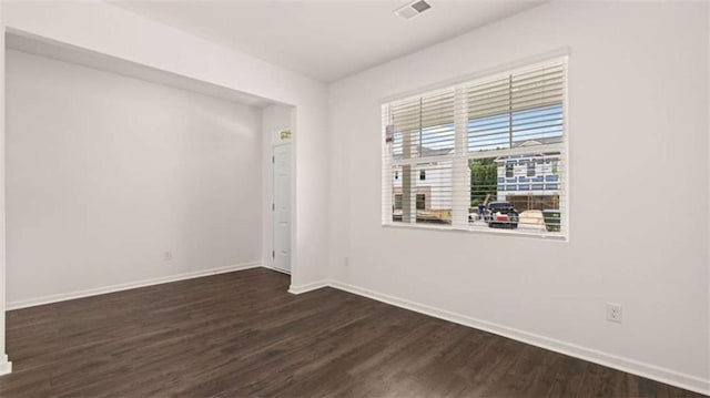 spare room featuring visible vents, baseboards, and dark wood-style floors