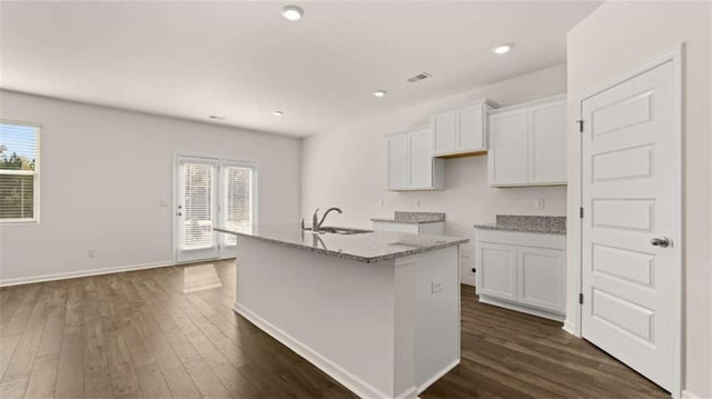 kitchen with light stone counters, dark hardwood / wood-style flooring, an island with sink, and white cabinets