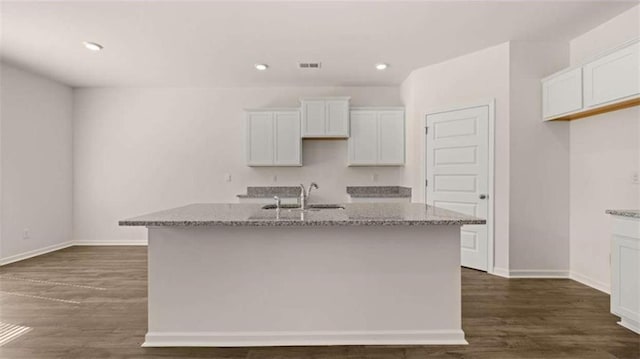 kitchen with dark wood-type flooring, a center island with sink, white cabinetry, and light stone countertops