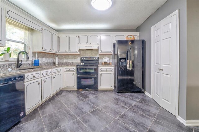 kitchen with dark tile patterned floors, black appliances, sink, decorative backsplash, and white cabinets