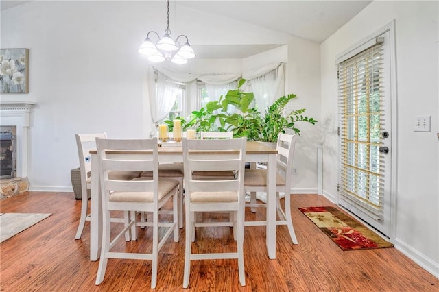 dining area featuring a fireplace, vaulted ceiling, hardwood / wood-style flooring, and a chandelier