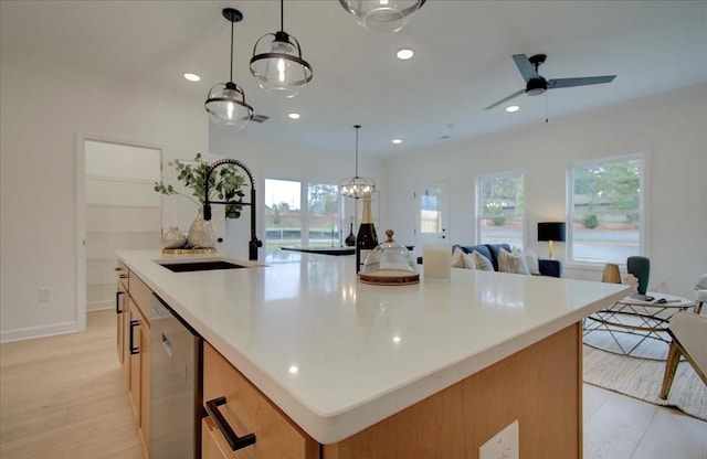 kitchen featuring open floor plan, a center island with sink, stainless steel dishwasher, light wood-style floors, and a sink