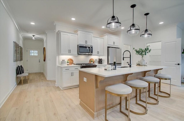 kitchen featuring light wood-type flooring, an island with sink, ornamental molding, a sink, and stainless steel appliances