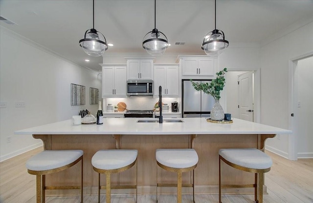 kitchen with a center island with sink, a sink, ornamental molding, appliances with stainless steel finishes, and light wood-type flooring